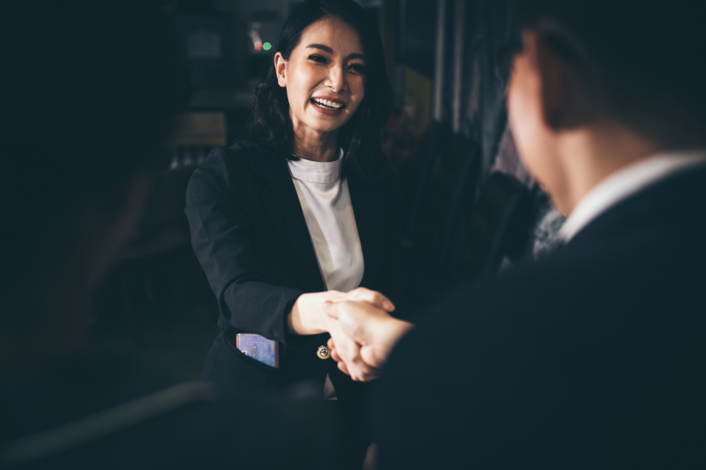 A woman and another person shaking hands in a professional setting, symbolizing agreement or collaboration.